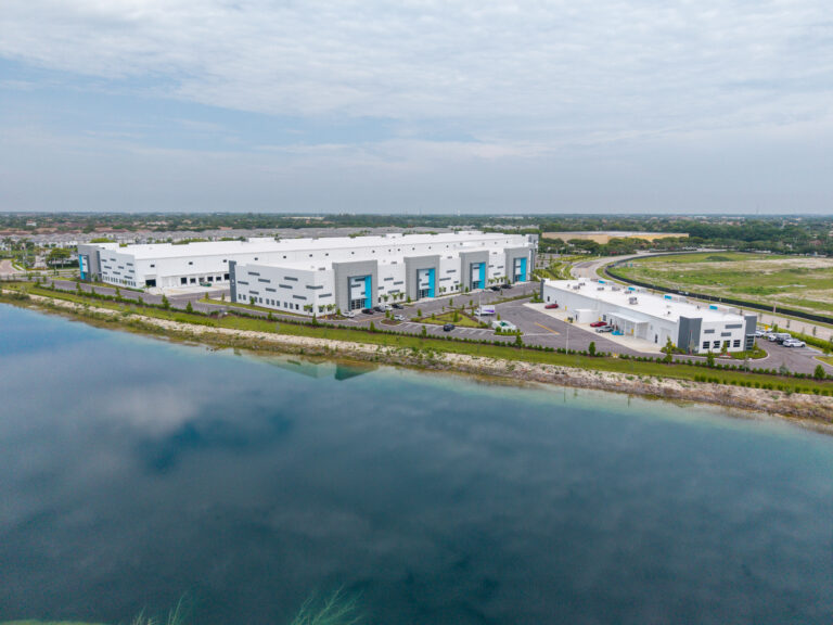Aerial view of two modern industrial warehouse buildings situated along a lakefront.
