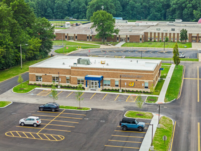 Aerial view of the Olmsted Falls City Schools administrative office building, featuring a parking lot with a few parked cars and a larger school building in the background.