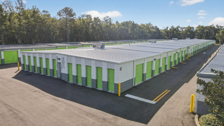 An aerial view of a self-storage facility featuring rows of white buildings with lime green roll-up doors.