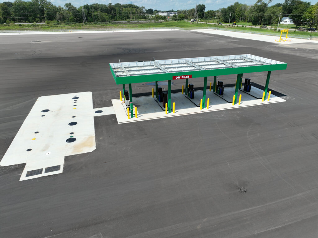 An aerial view of a green-roofed fuel station with a designated “Off Road” pump located in a large, empty asphalt lot.