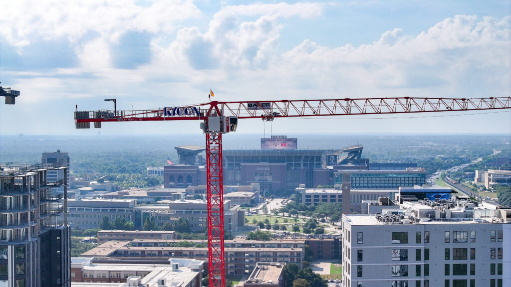 A tall red construction crane stands in front of Kyle Field stadium on the Texas A&M University campus.