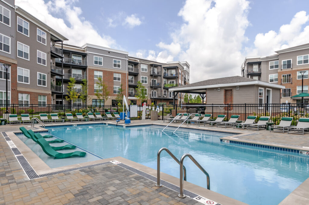 Apartment complex swimming pool with lounge chairs and a pool house.