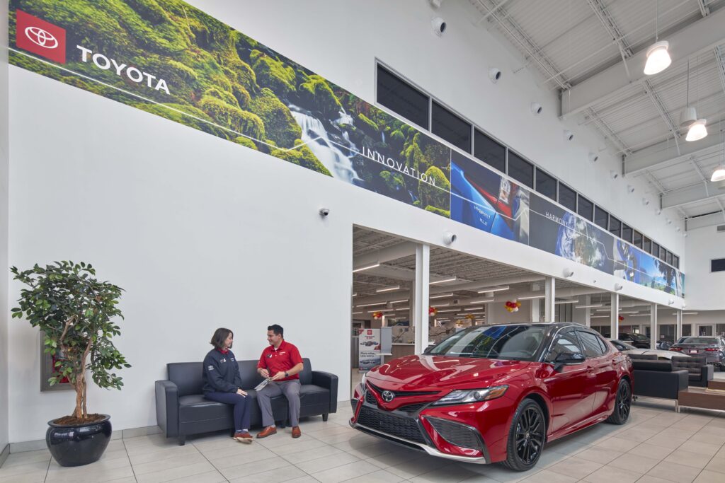 A Toyota dealership showroom with a red sedan on display and two employees sitting on a black sofa.