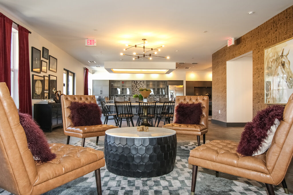 Four tan leather chairs with dark pillows arranged around a circular black coffee table in a modern lounge area.