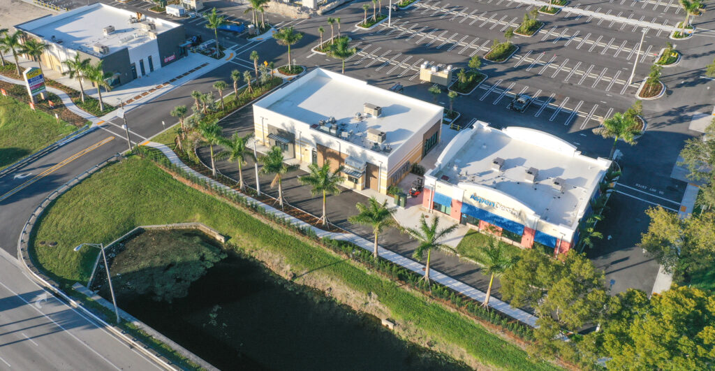 Aerial view of two commercial buildings with parking lots next to a pond and road.
