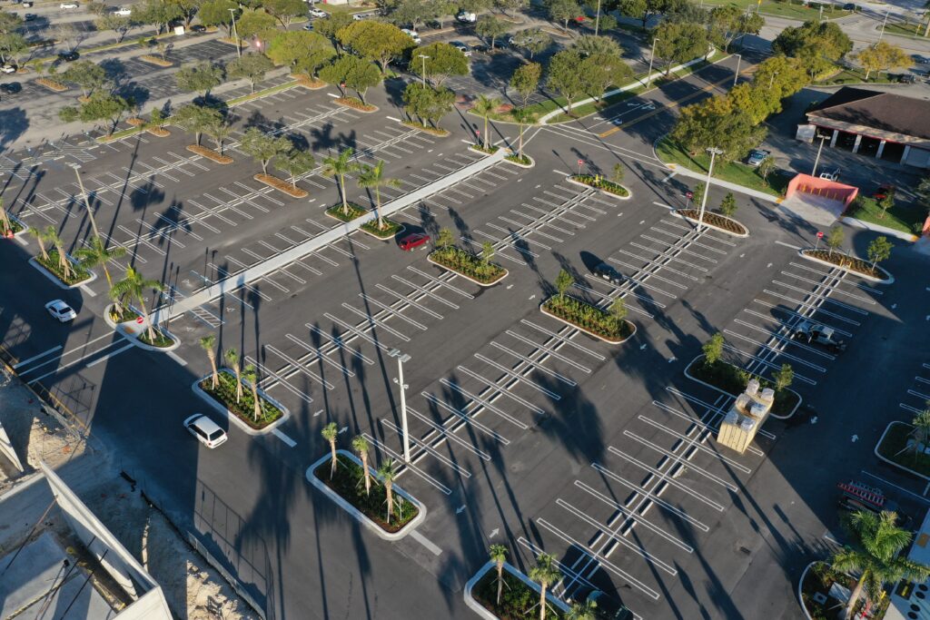 Aerial view of a mostly empty parking lot with palm tree islands and scattered cars.