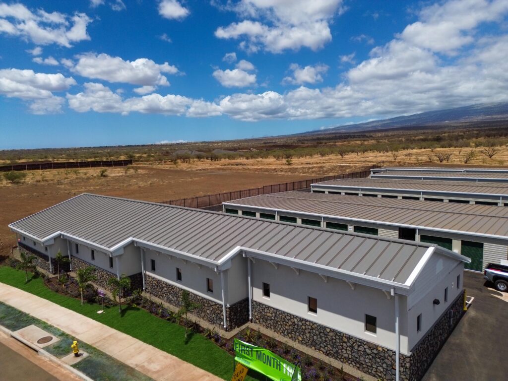 Aerial view of a self-storage facility with several long, metal-roofed buildings and a sign advertising “First Month Free.”