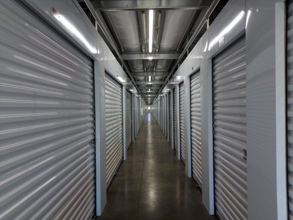 A long hallway in a self-storage facility lined with closed metal roll-up doors.