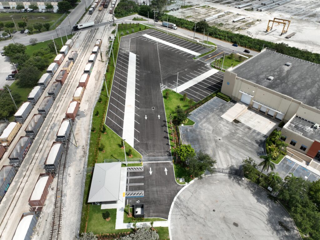 Aerial view of a parking lot next to a commercial warehouse and a set of railroad tracks carrying freight cars.