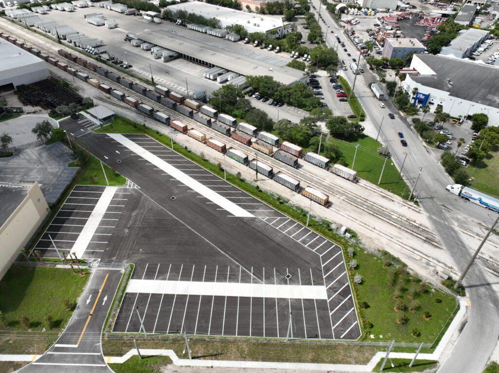 Aerial view of a parking lot next to a railway line with freight cars and a nearby industrial road.