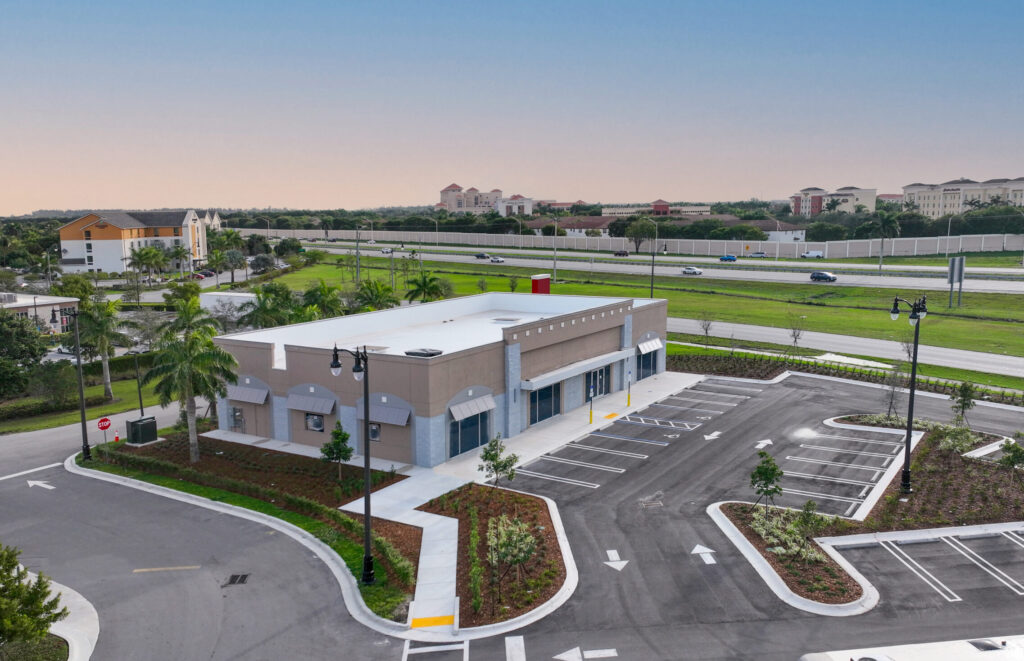 An aerial view of a modern, vacant commercial building with an empty parking lot next to a highway.