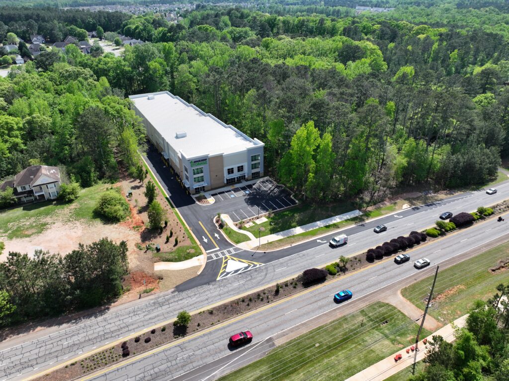 Aerial view of a self-storage facility bordered by woods and a road with passing traffic.