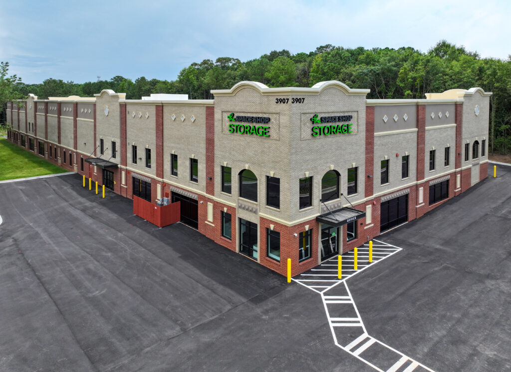 Aerial view of a two-story beige and red brick building labeled “Space Shop Storage” with a parking lot in the foreground.