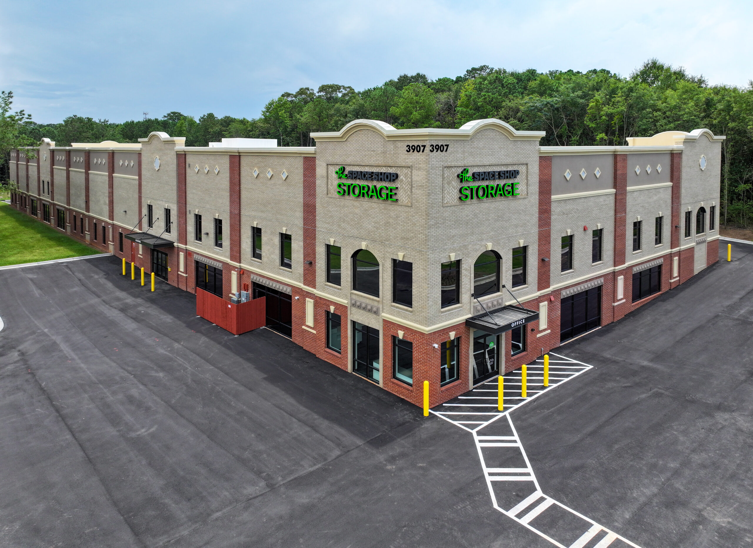 Aerial view of a two-story beige and red brick building labeled “Space Shop Storage” with a parking lot in the foreground.