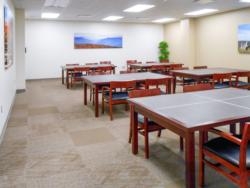 A meeting room with several dark wood tables and chairs arranged in rows, with landscape prints hanging on the white walls.