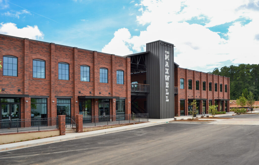 A two-story red brick building with the vertical sign “The Maxwell” on its dark metal center tower.