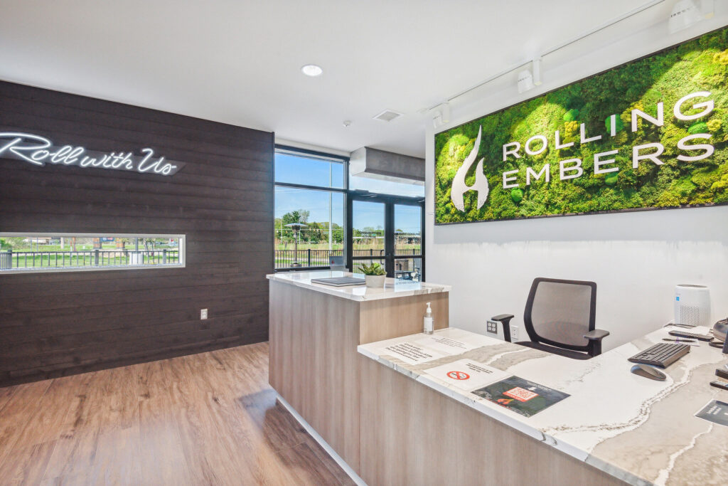 Reception desk in an office with a moss wall logo sign for Rolling Embers and a neon sign reading “Roll with Us.”