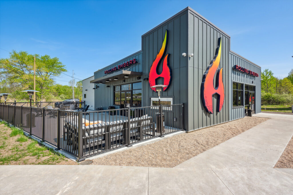 Exterior of the Rolling Embers restaurant building featuring large flame-shaped signage and an outdoor patio with seating.