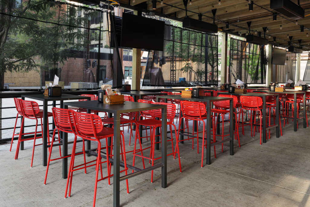 Outdoor patio seating with rows of high-top tables and bright red stools.