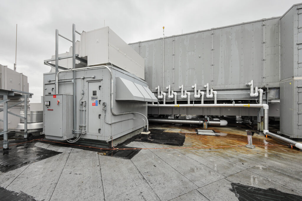 Rooftop HVAC unit with attached piping and electrical conduits on a flat membrane roof.