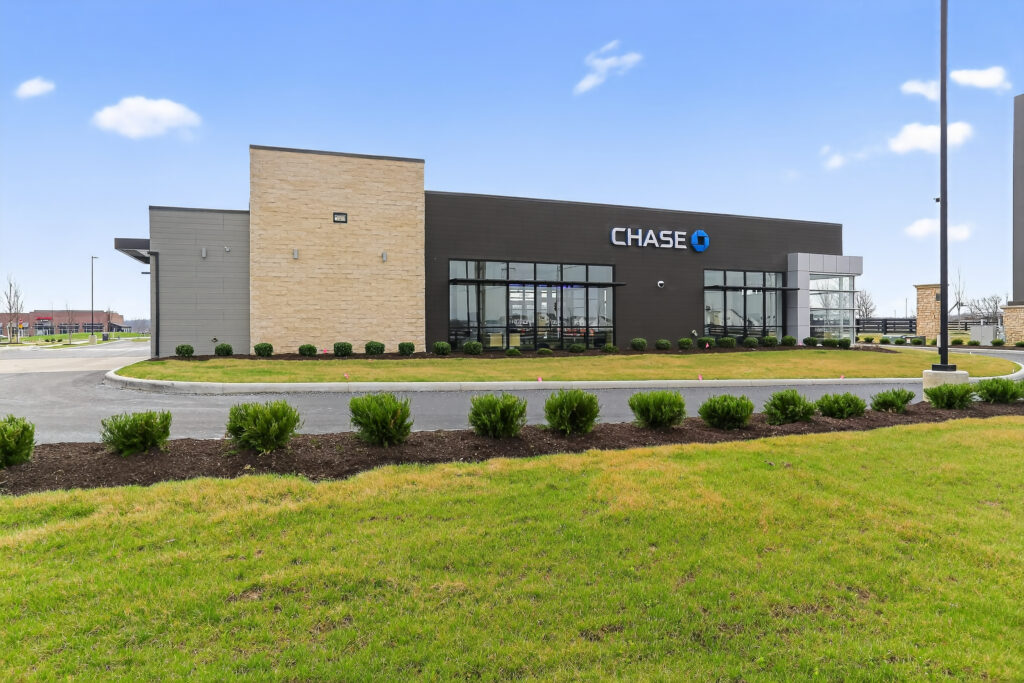 A Chase bank branch building with a stone and dark brown facade, situated behind a manicured lawn and parking lot.