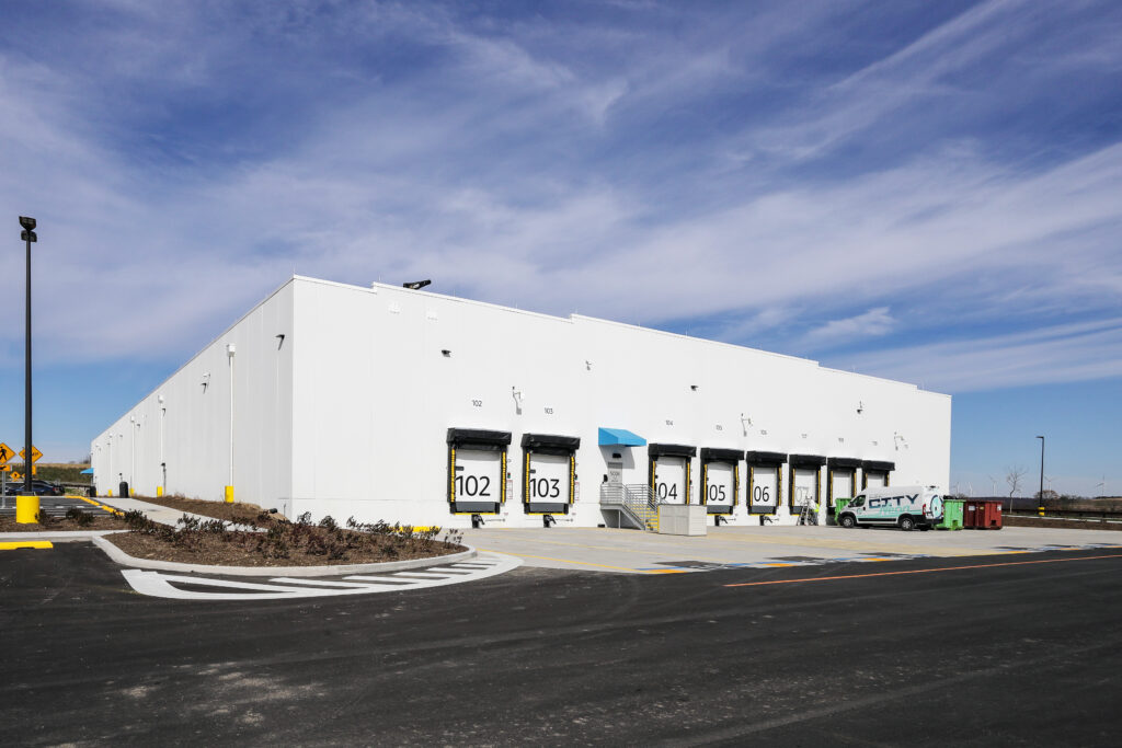 A white warehouse building featuring multiple loading docks numbered 102 through 107 and a parked utility van.