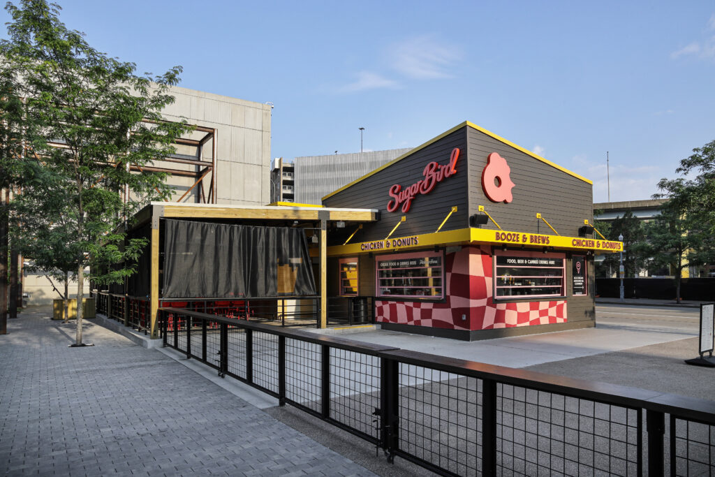 Sugar Bird restaurant exterior featuring a covered patio and a storefront with signage for chicken, donuts, and booze.