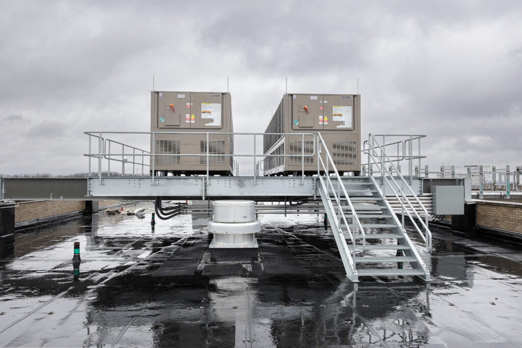 Two York HVAC units mounted on a metal platform with a stairway on a flat roof.
