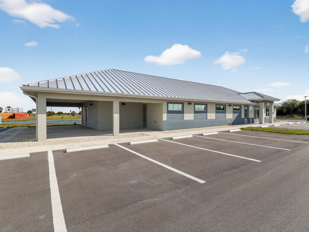 A single-story commercial building with a metal roof and a covered entryway, viewed from a parking lot.