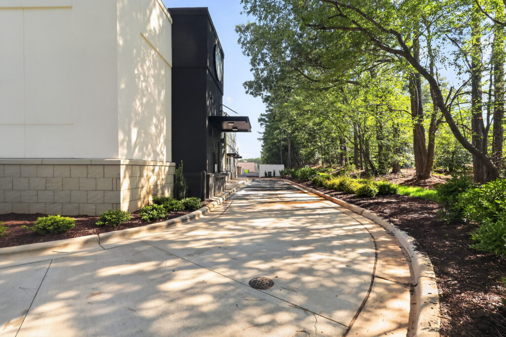 A curving concrete drive-thru lane beside a commercial building, shaded by trees.