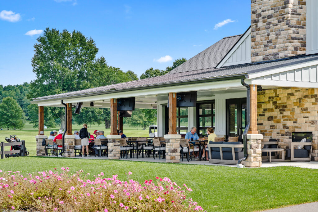 People dining on the covered outdoor patio of a clubhouse overlooking a golf course.