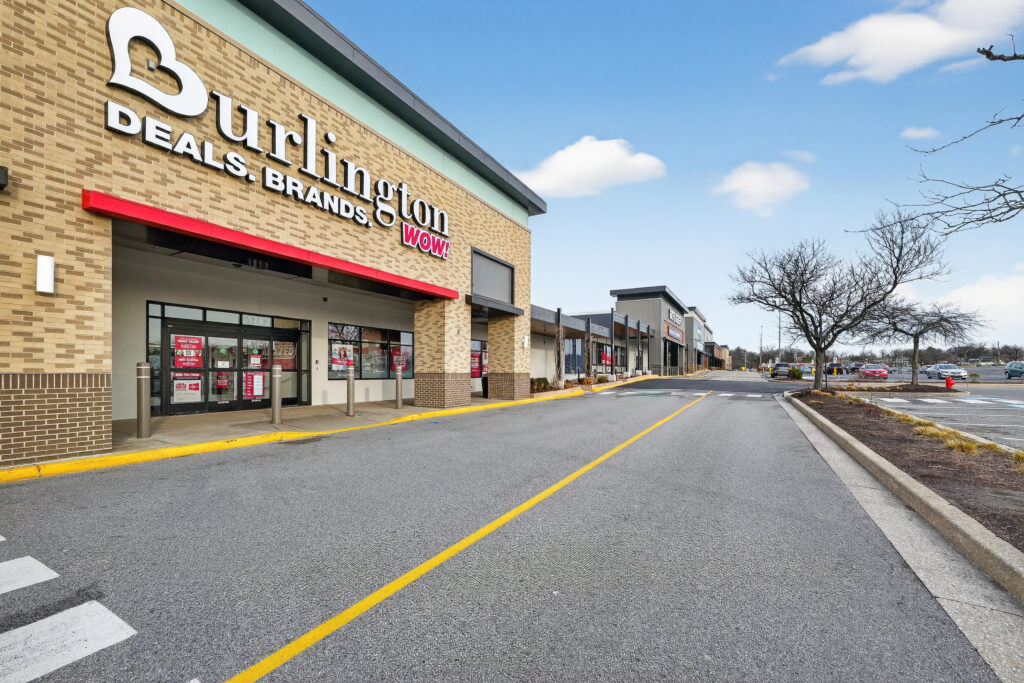 Burlington store entrance in a strip mall with a parking lot in the foreground.