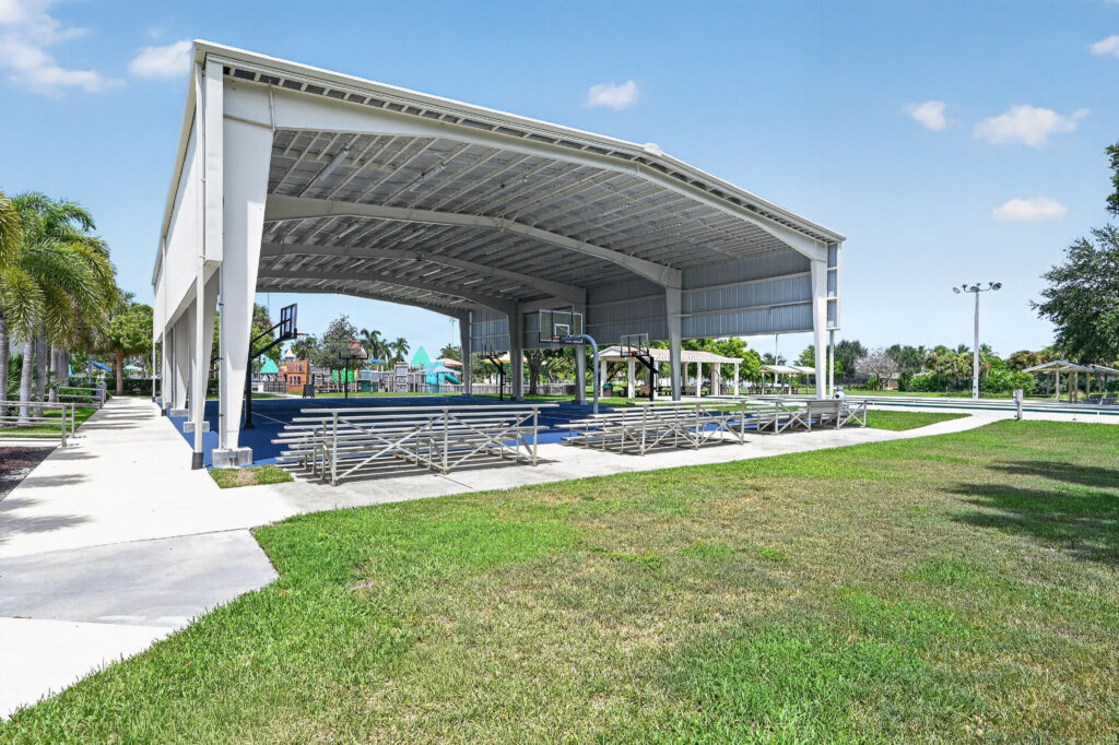 A covered outdoor basketball court with metal bleachers on a sunny day.