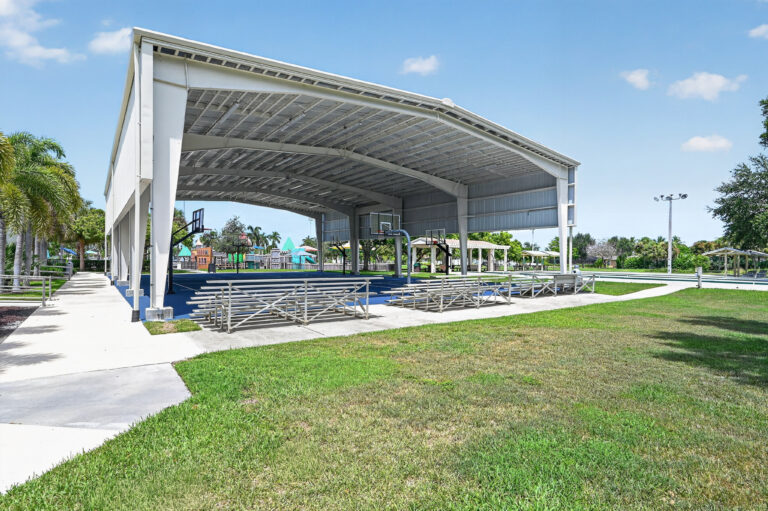 A covered outdoor basketball court with metal bleachers on a sunny day.