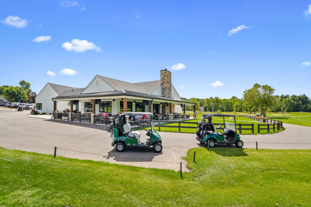 Two golf carts parked on a paved path in front of a clubhouse with an outdoor patio.