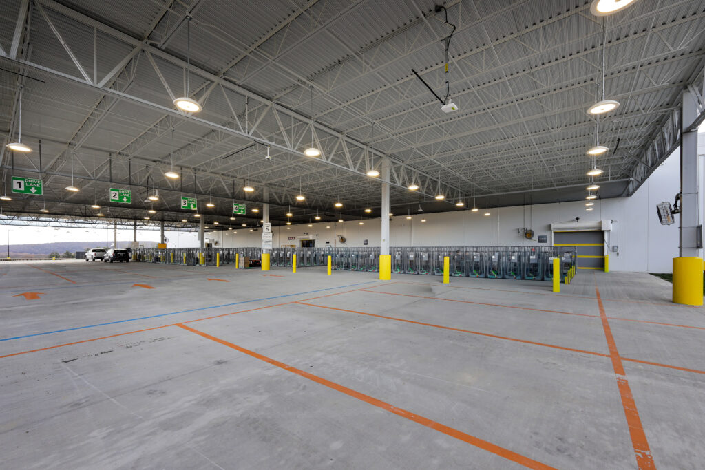 A large, covered outdoor loading area with numbered drive lanes and rows of metal storage cages on a concrete lot.