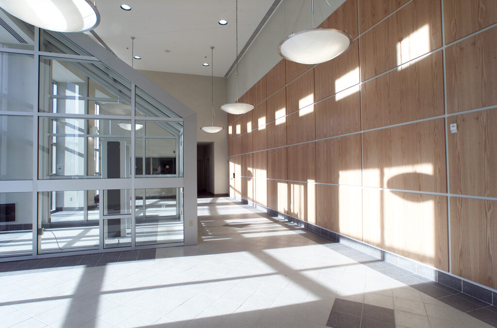 Modern hallway with a glass-enclosed office, wood-paneled walls, and circular pendant lighting.