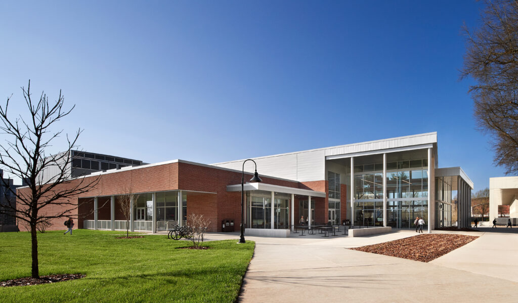 Modern building with a brick and glass facade, adjacent to a green lawn, a paved walkway, and a clear blue sky.
