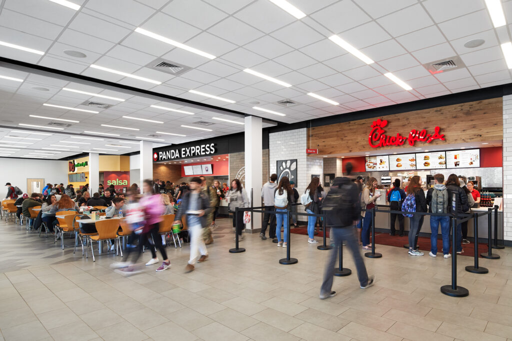 People eating and waiting in line at a food court featuring a Panda Express and a Chick-fil-A.