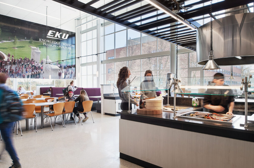 Students dining in a bright, modern university cafeteria with a large EKU banner on the wall.