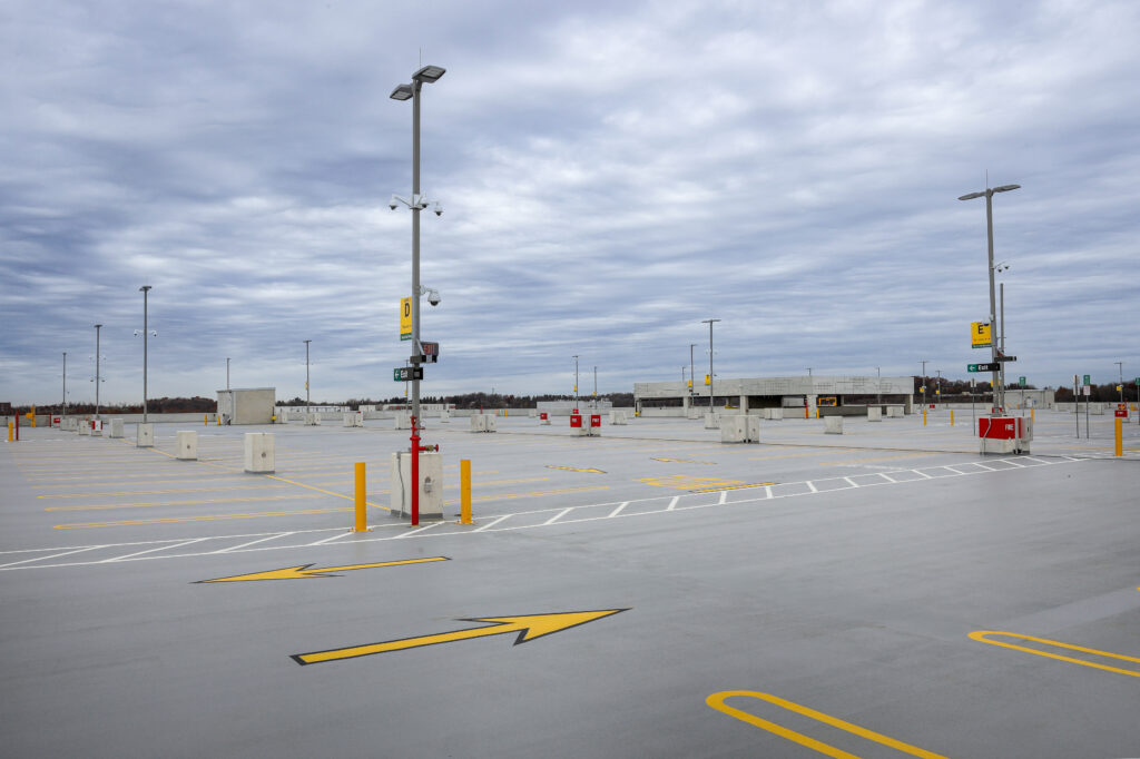 An empty outdoor parking lot with yellow painted arrows and parking space markings under a cloudy sky.