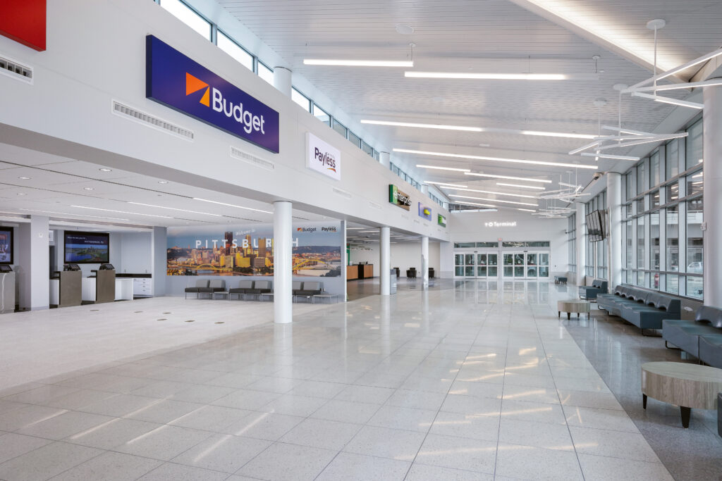 An airport terminal interior featuring a row of car rental agency counters beneath signs for Budget, Payless, and Enterprise.
