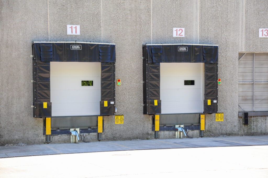 Two warehouse loading dock bays numbered 11 and 12, each with a white door, black dock seal, and safety signage.
