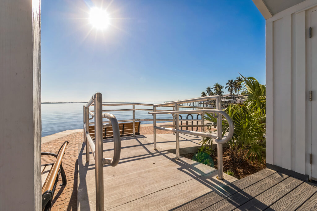A wooden ramp with metal railings leading to a waterfront overlook with a bench.