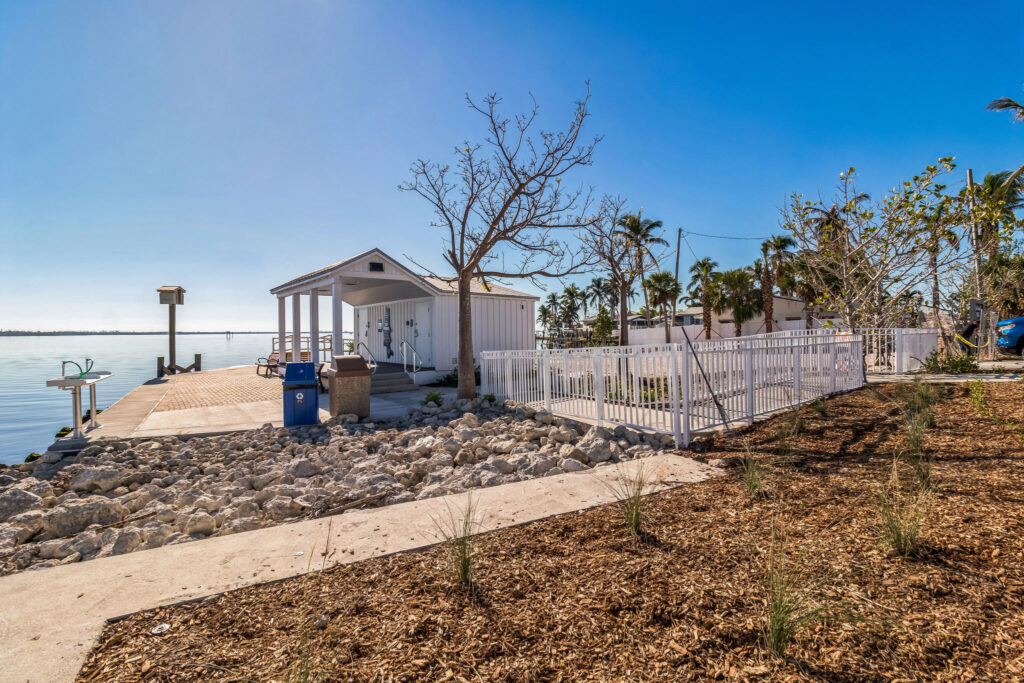 A white boat house with a covered patio located on a concrete dock next to a calm body of water.