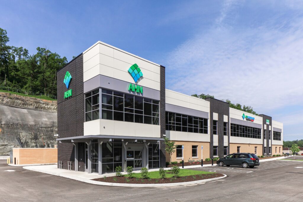 Exterior view of an AHN medical office building with a parking lot and a rock embankment in the background.
