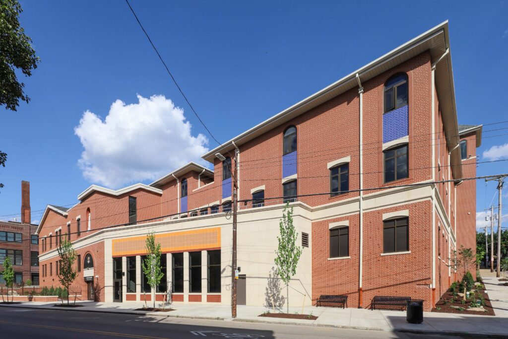 A low-angle view of a brick commercial building with a tan stone base, featuring large windows and blue decorative panels.