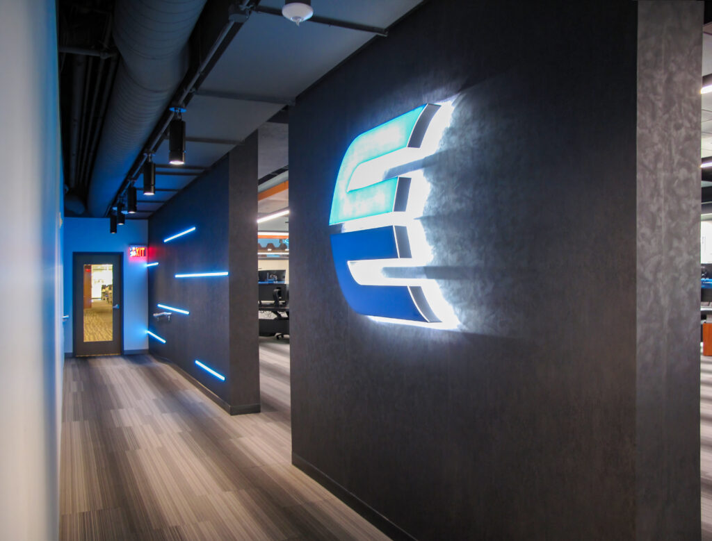 A brightly lit, glowing blue logo on a dark office wall in a modern hallway.