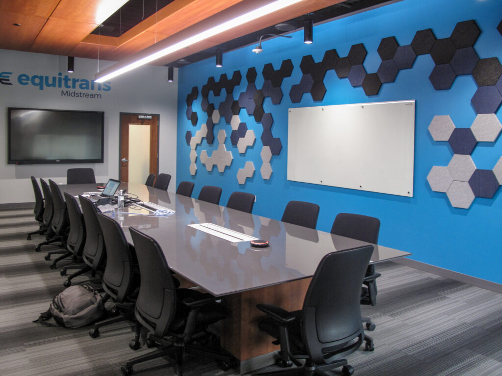 Conference room with a long table, black chairs, a wall-mounted monitor with the Equitrans Midstream logo, and a whiteboard surrounded by blue and grey hexagonal acoustic tiles.