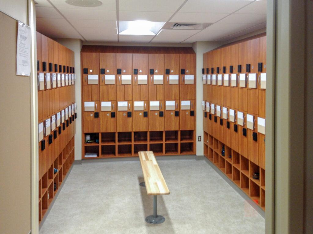 A locker room featuring three walls of wood-look lockers with digital keypads and an open bench in the center.